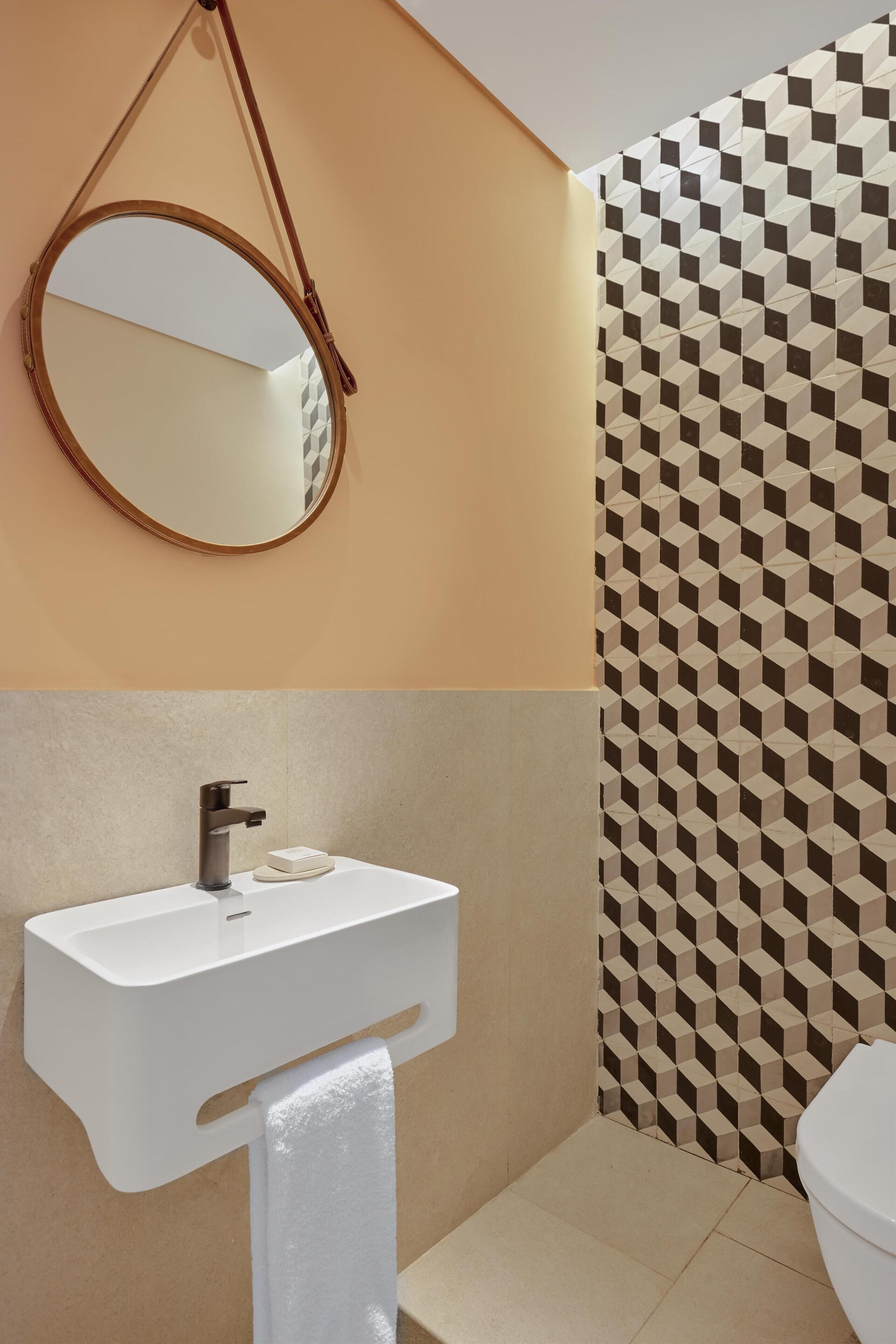 Une salle de bain avec un lavabo blanc, un miroir et un mur à motifs.