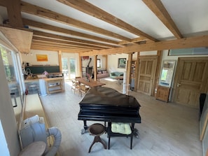 Enjoy a comfortable living space with a grand piano, dining table, and sofa, connected to an outdoor area through a sliding glass door.
