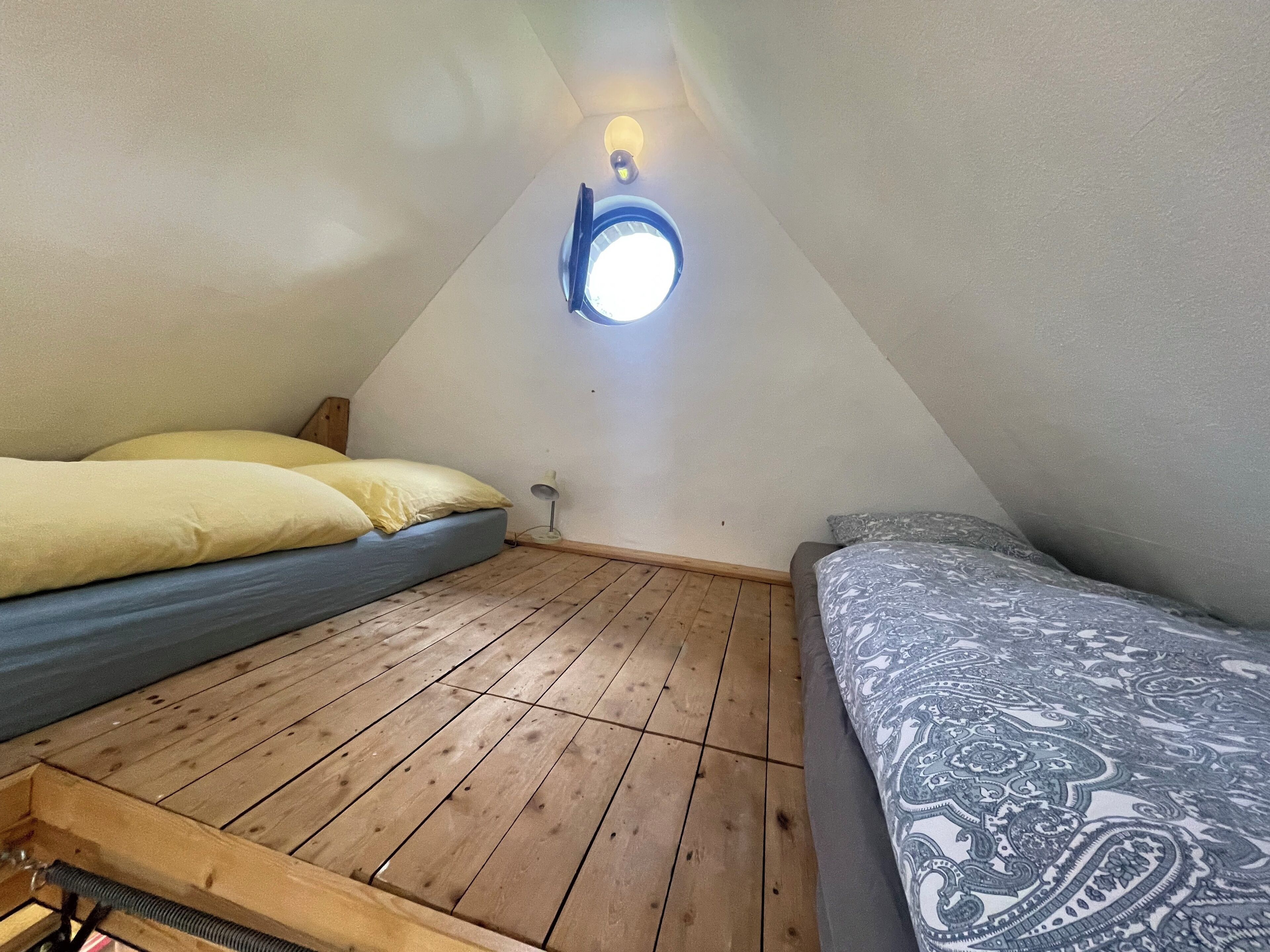 A small, cozy attic bedroom with a sloped ceiling, wooden flooring, and two beds with different bedding.