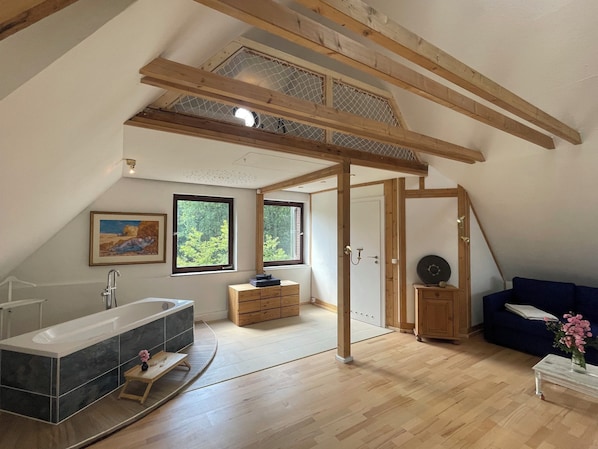 Amplio dormitorio tipo loft con un gran tragaluz, bañera integrada y una zona de estar acogedora.
