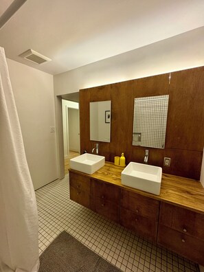A modern bathroom with two sinks, wooden vanity, large mirrors, and a shower curtain. - Mid-Century Retreat in the Heart of Encinitas (Encinitas)