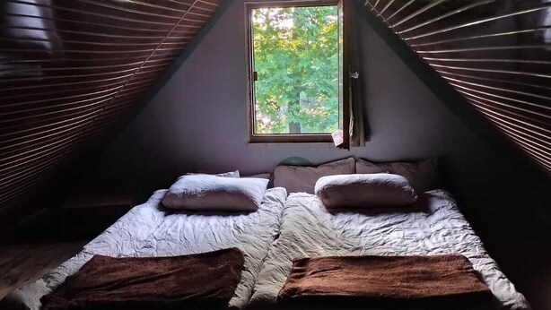 Une chambre mansardée chaleureuse avec un plafond en pente, une fenêtre donnant sur les arbres, un lit avec des oreillers et une couverture.