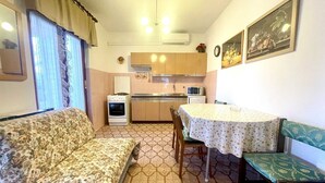 A compact living space with a sofa, a dining table with chairs, a kitchenette, and a patterned floor.