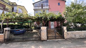 A residential building with a gated entrance, a balcony, and a covered area with plants.