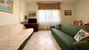 A cozy living room with a sofa, a TV, and a painting on the wall.