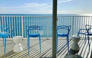 Un balcón con sillas azules y taburetes blancos, con vista al mar.