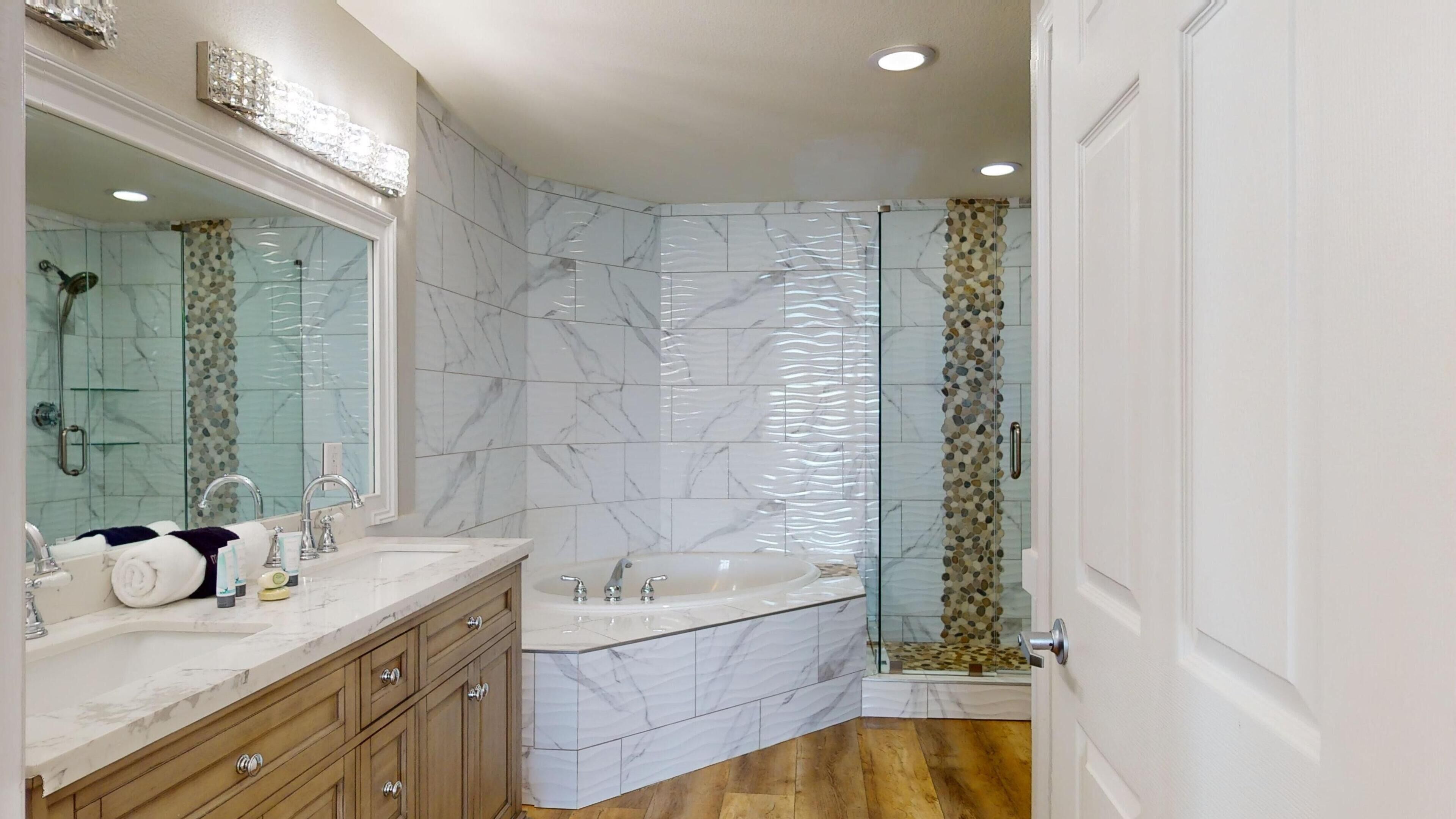 A modern bathroom with a marble vanity, a freestanding bathtub, and a glass shower enclosure.