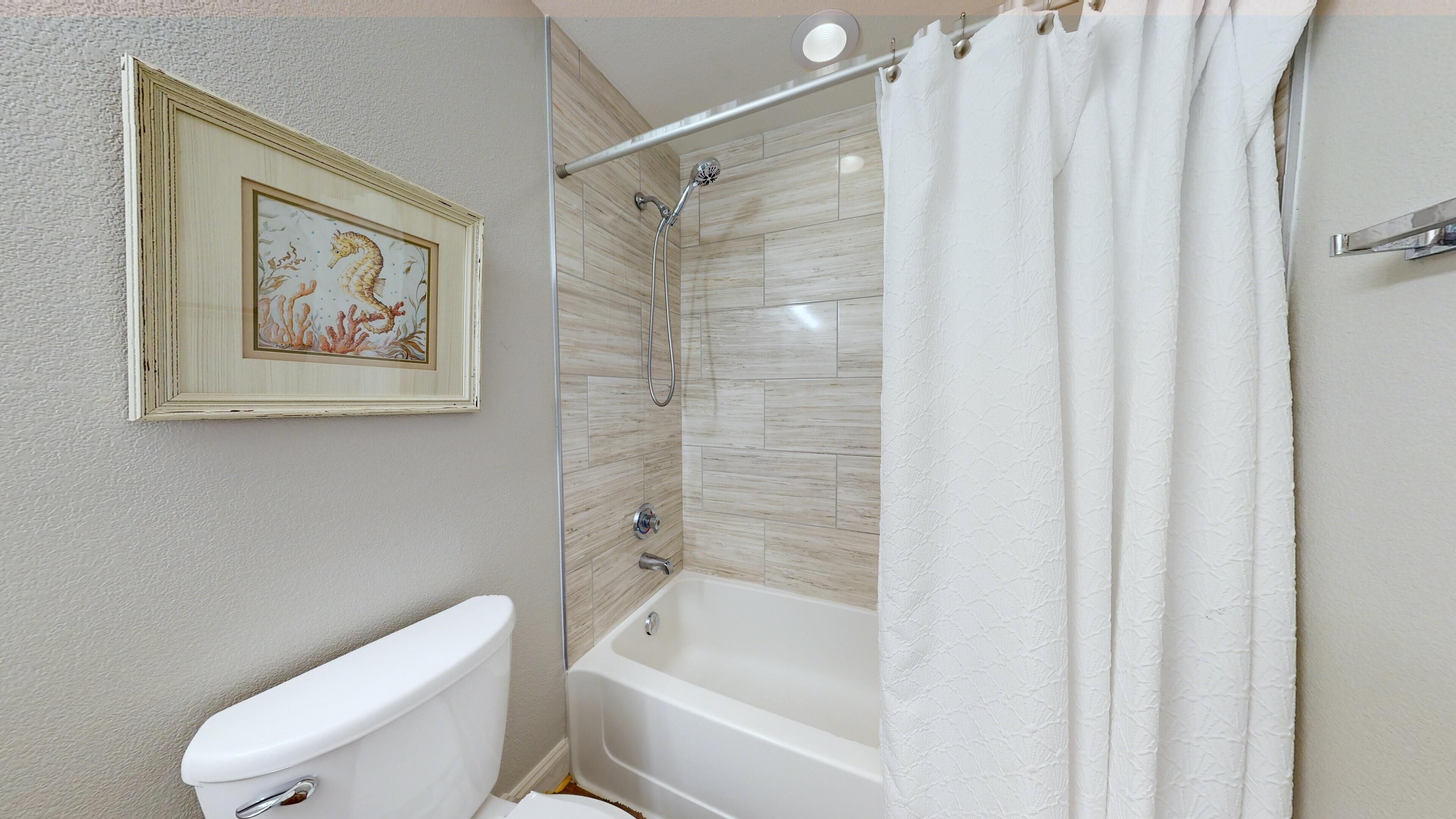 A bathroom with a toilet, a bathtub, and a shower. There is a framed picture on the wall.