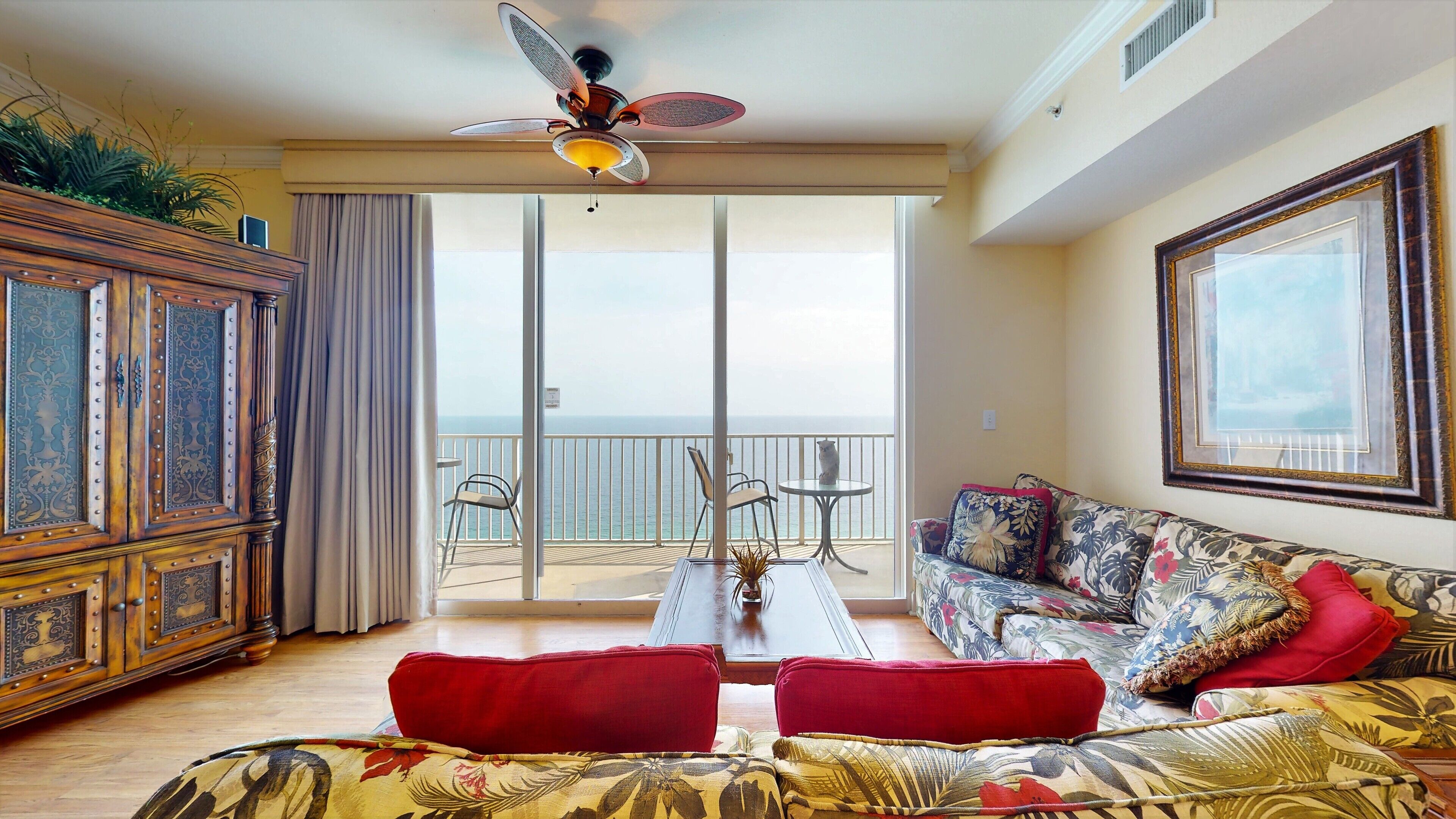 A spacious living room with a balcony, a ceiling fan, and a large window.