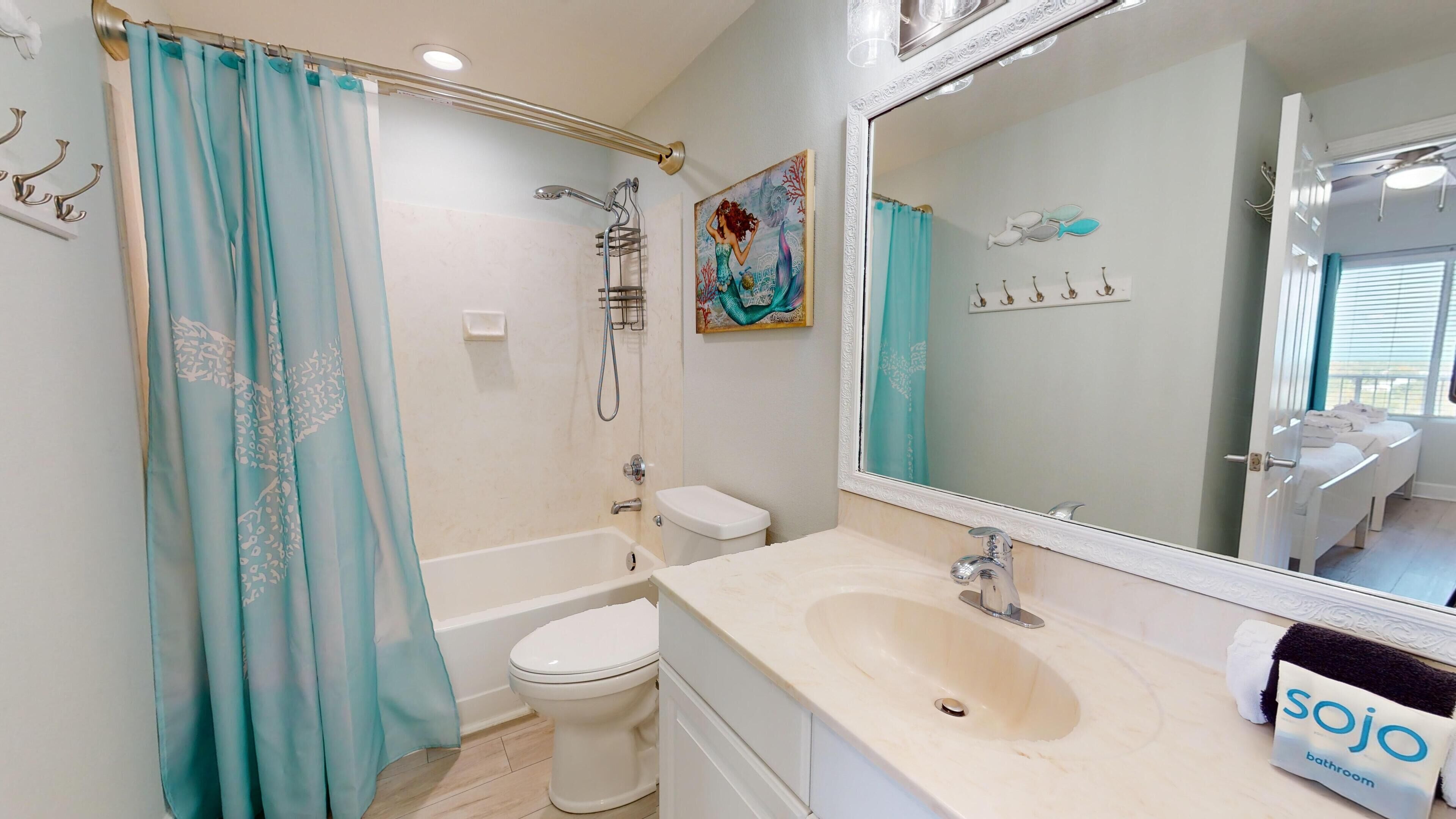 A bathroom with a bathtub, toilet, and sink. There is a shower curtain, a painting on the wall, and a towel rack.