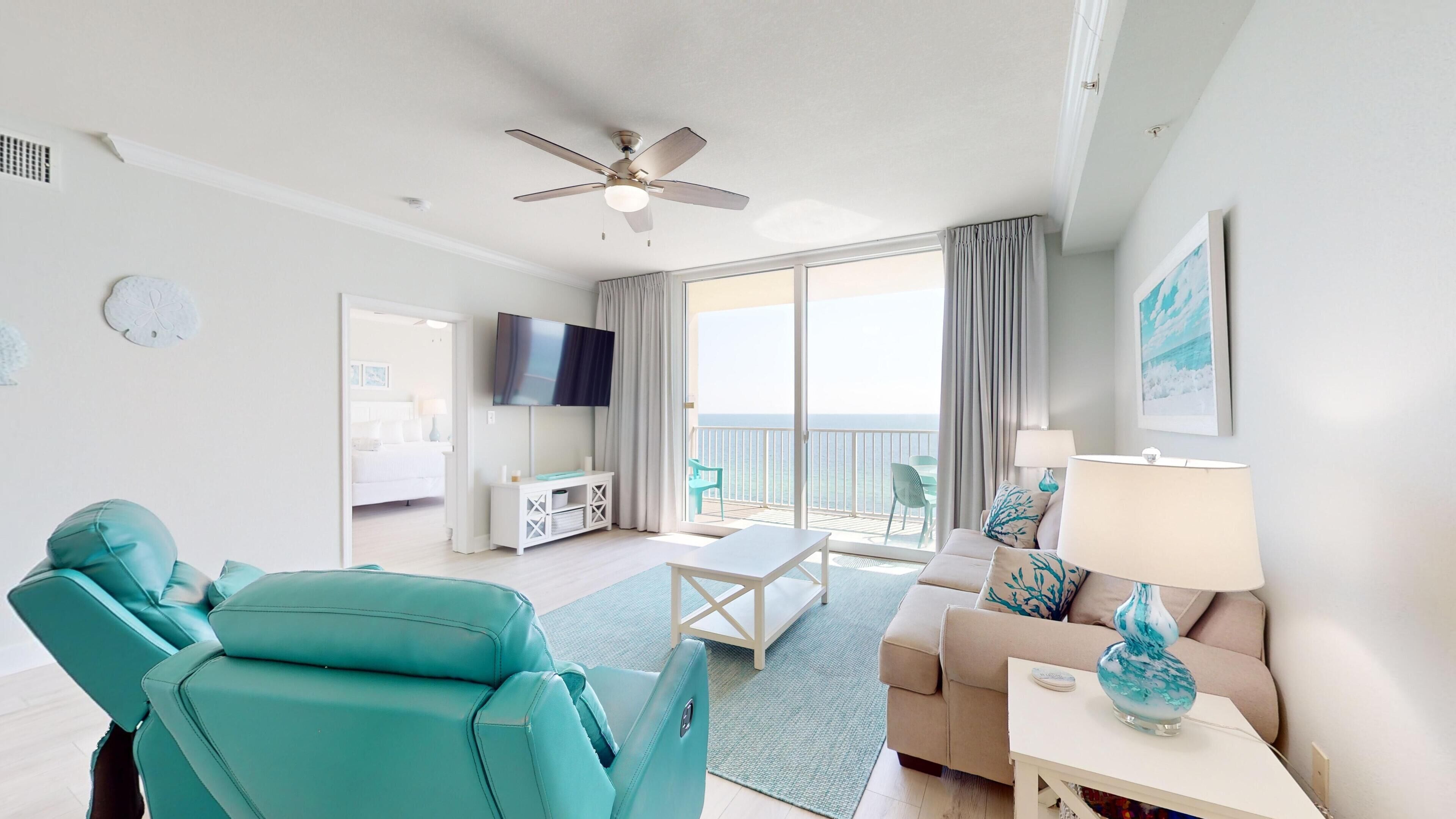 A modern hotel room with a balcony, a ceiling fan, a flat-screen TV, and a sofa with a view of the ocean.
