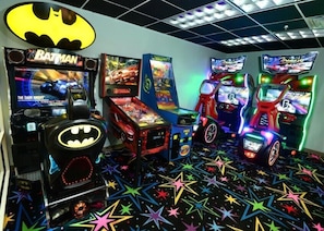 A gaming arcade with various machines, including a Batman-themed one, and a ceiling with a grid pattern. - Tidewater Beach Resort by Gibson BR (Panama City Beach)