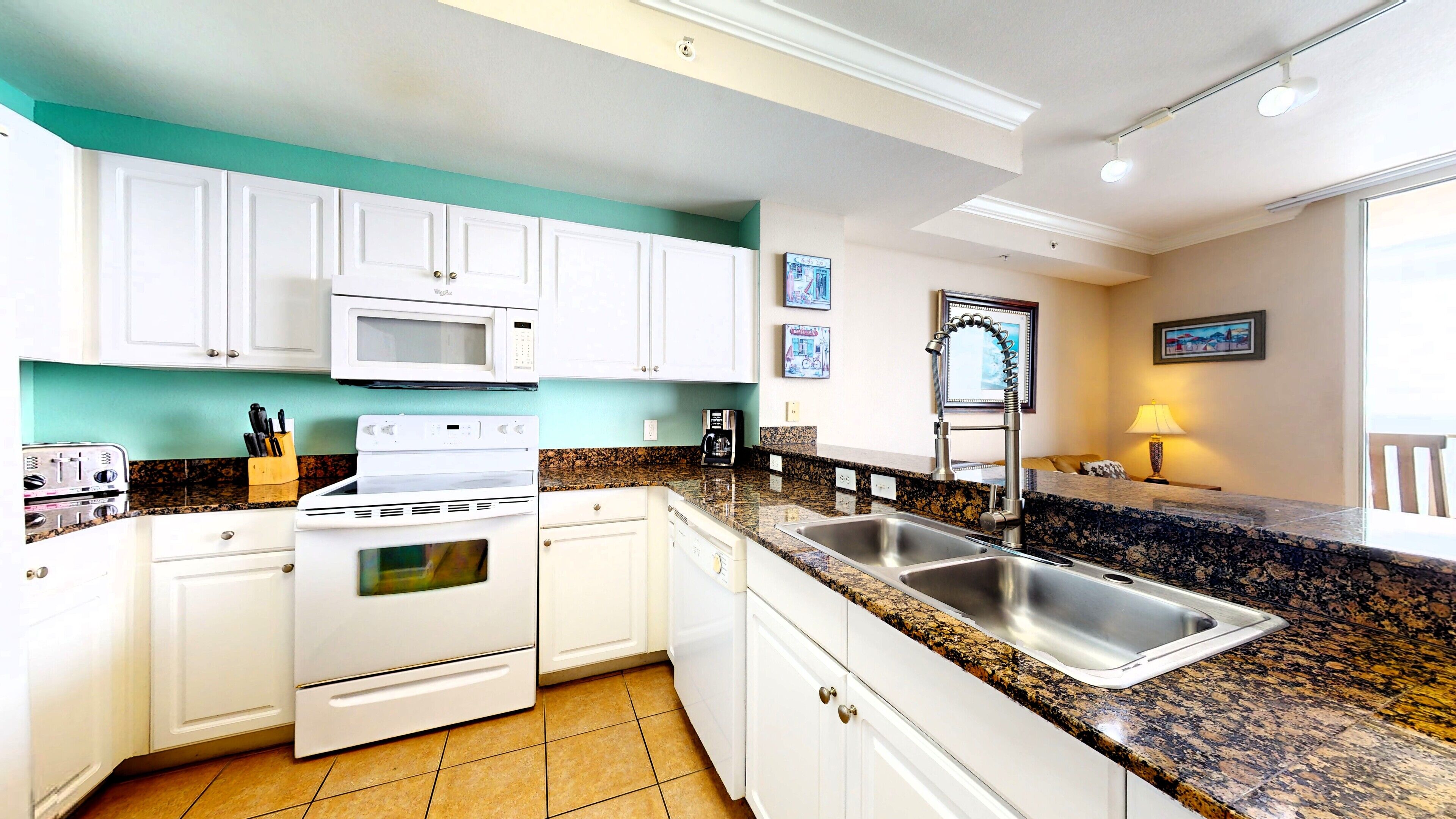 A kitchen with white cabinets, a stove, a microwave, a sink, and a coffee maker.