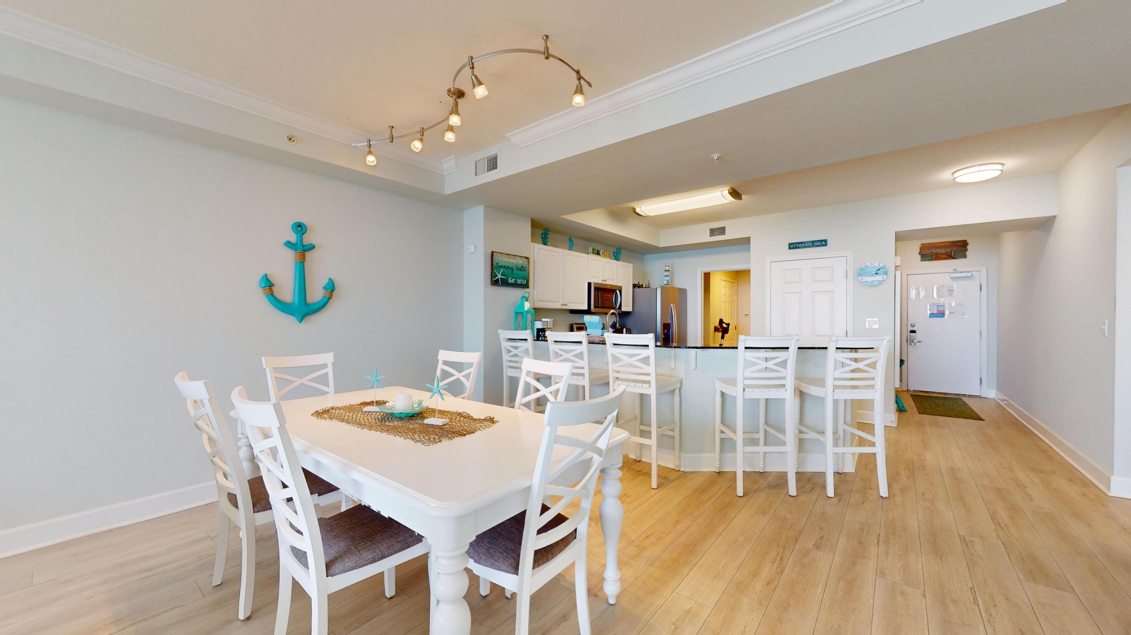A modern kitchen with white cabinetry, a central island, and a dining area with white chairs and a table.