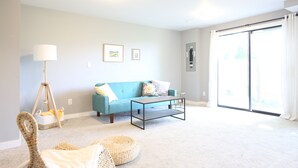 Ein Wohnzimmer mit einem blauen Sofa, einem Couchtisch, einer Katzenliege und einer großen Schiebeglastür.