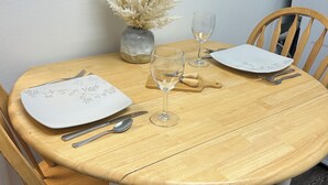 Une table à manger ornée d’un vase de fleurs séchées, de deux verres à vin et de couverts.