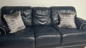 Un canapé en cuir noir agrémenté de coussins à franges, une tapisserie murale à motifs et un tapis à motifs.