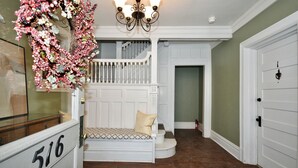 A staircase leading to a second-floor landing with a white railing, a chandelier, and a door with a number plaque. - Fun Retro Apartment on Quiet Dead End Street Near Stage AE & Acrisure Stadium (Pittsburgh)