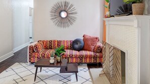 A living room with a patterned sofa, a coffee table, a decorative mirror, and a fireplace. - Fun Retro Apartment on Quiet Dead End Street Near Stage AE & Acrisure Stadium (Pittsburgh)