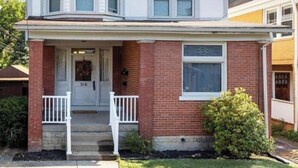 A two-story house with a gabled roof, a front porch, and a brick facade. - Fun Retro Apartment on Quiet Dead End Street Near Stage AE & Acrisure Stadium (Pittsburgh)