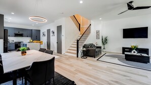 A modern interior with a dining area, kitchen, staircase, living room, and a flat-screen TV.