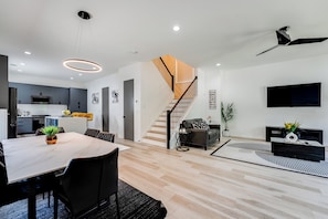 A modern interior with a dining area, kitchen, staircase, living room, and a flat-screen TV.