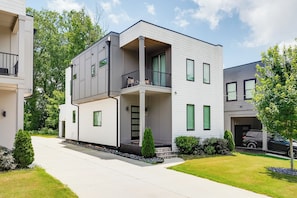 Ein modernes Wohngebäude mit zwei Etagen, einem Balkon, einer Garage und einem gepflegten Rasen.