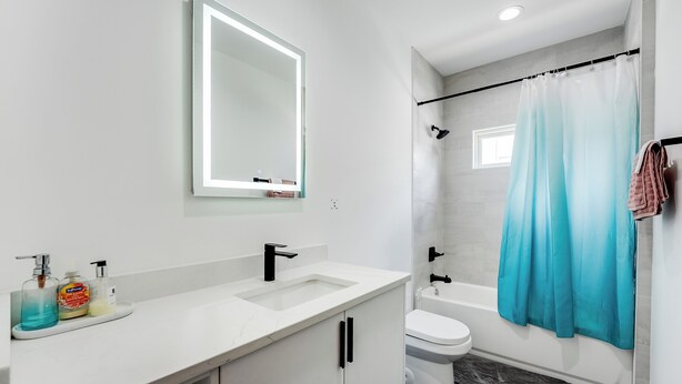 A modern bathroom with a white sink, a mirror with lights, a toilet, and a shower curtain.