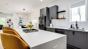 A modern kitchen with a central island, grey cabinets, and a large window.