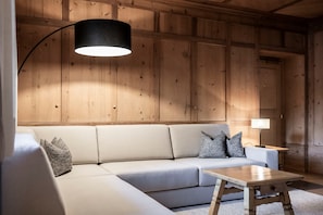 A room with a sofa, a table, a lamp, and wooden paneling on the walls. - Apartment 'Appartamento Stube' with Mountain View, Private Terrace and Wi-Fi (Ortisei)