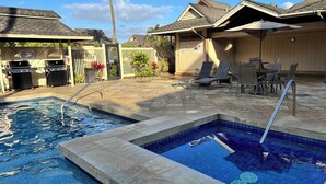 A swimming pool with two separate sections, a patio area with lounge chairs, and a barbecue setup. - Air Conditioned Upstairs Condo with full kitchen, pool, wifi, walk to beach. (Princeville)