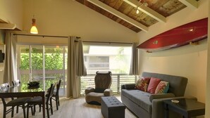 A spacious living area with a wooden ceiling, a red canoe, a grey sofa, and a dining table with chairs. - Air Conditioned Upstairs Condo with full kitchen, pool, wifi, walk to beach. (Princeville)