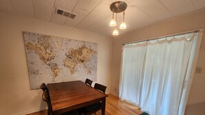 Un comedor con una mesa y sillas de madera, un mapa del mundo en la pared y una ventana con cortinas blancas.