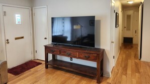 Un pasillo con piso de madera, un televisor sobre un pedestal de madera y una alfombra roja.