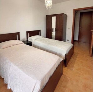Two single beds with white bedspreads, a large wardrobe with mirror, and a door to an adjacent room.