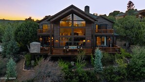 Une grande maison en bois à plusieurs étages, dotée d’un balcon au deuxième étage et entourée d’arbres denses.