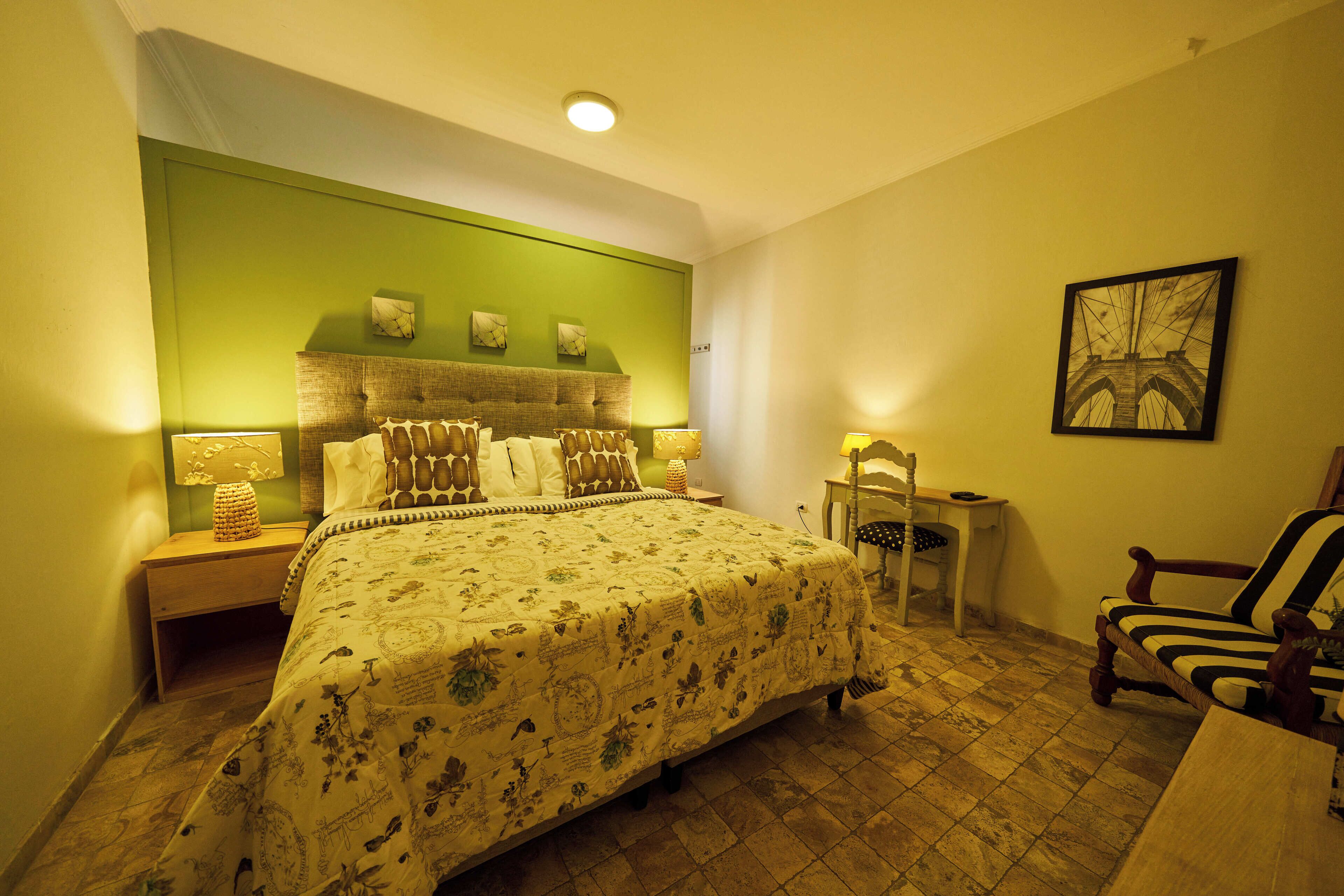 A bedroom with a large bed, a nightstand, a chair, and a small table.
