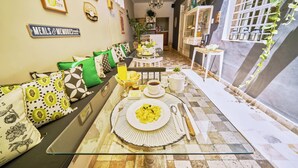 Comedor con una mesa de vidrio dispuesta para dos personas, rodeado de cojines estampados y un suelo a cuadros.