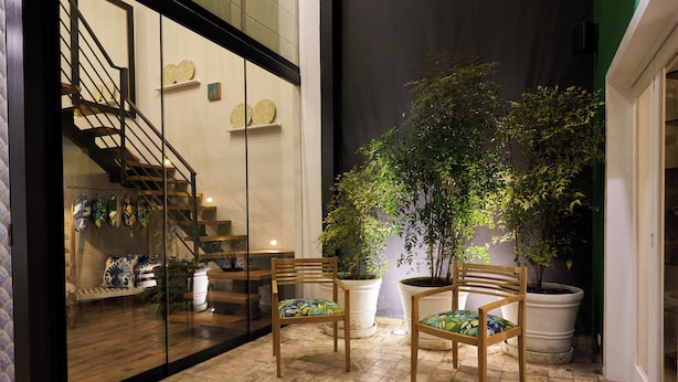 Un espacio interior amplio con suelo de baldosas, dos sillas de madera y grandes macetas con plantas.