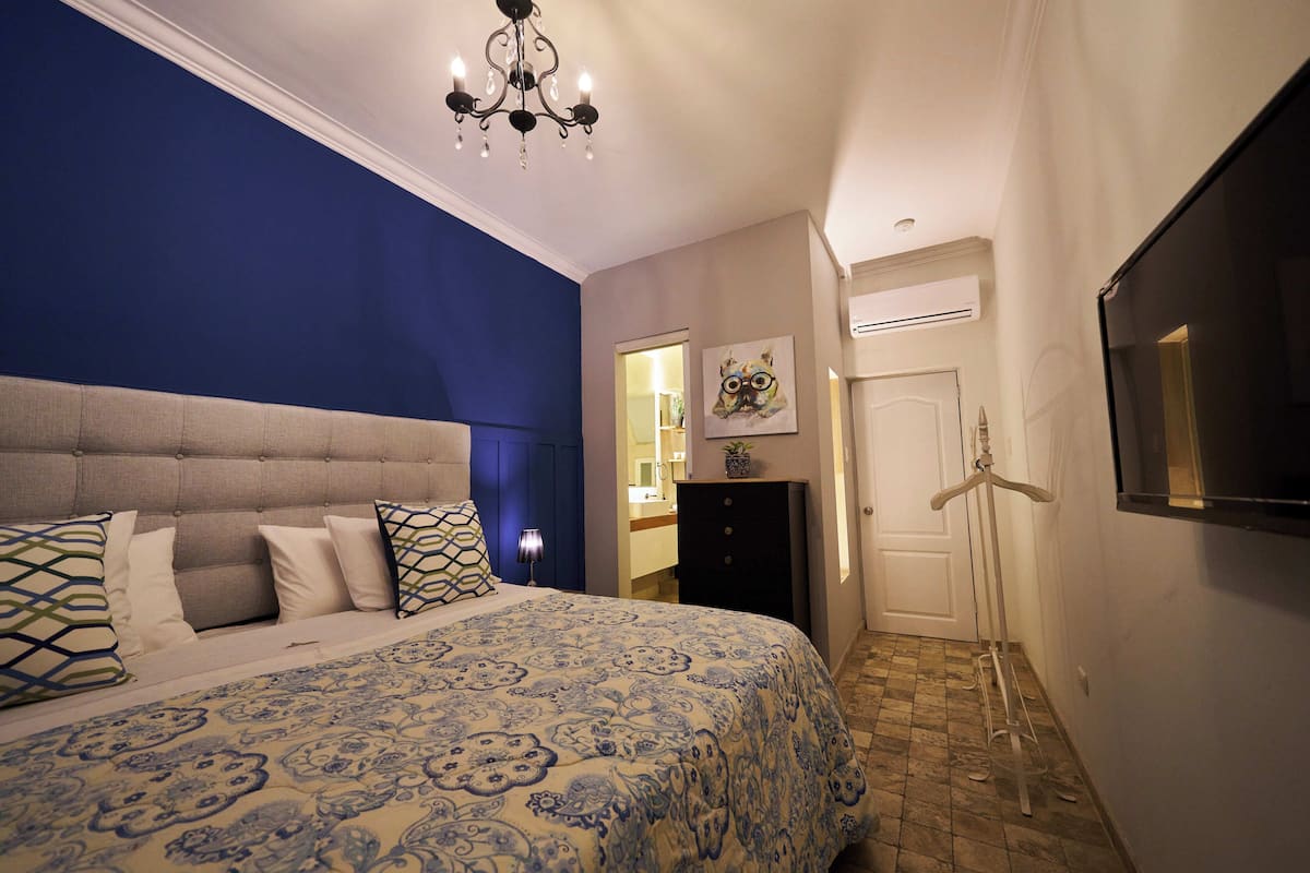 A bedroom with a large bed, a dresser, a mirror, a coat rack, and a TV.