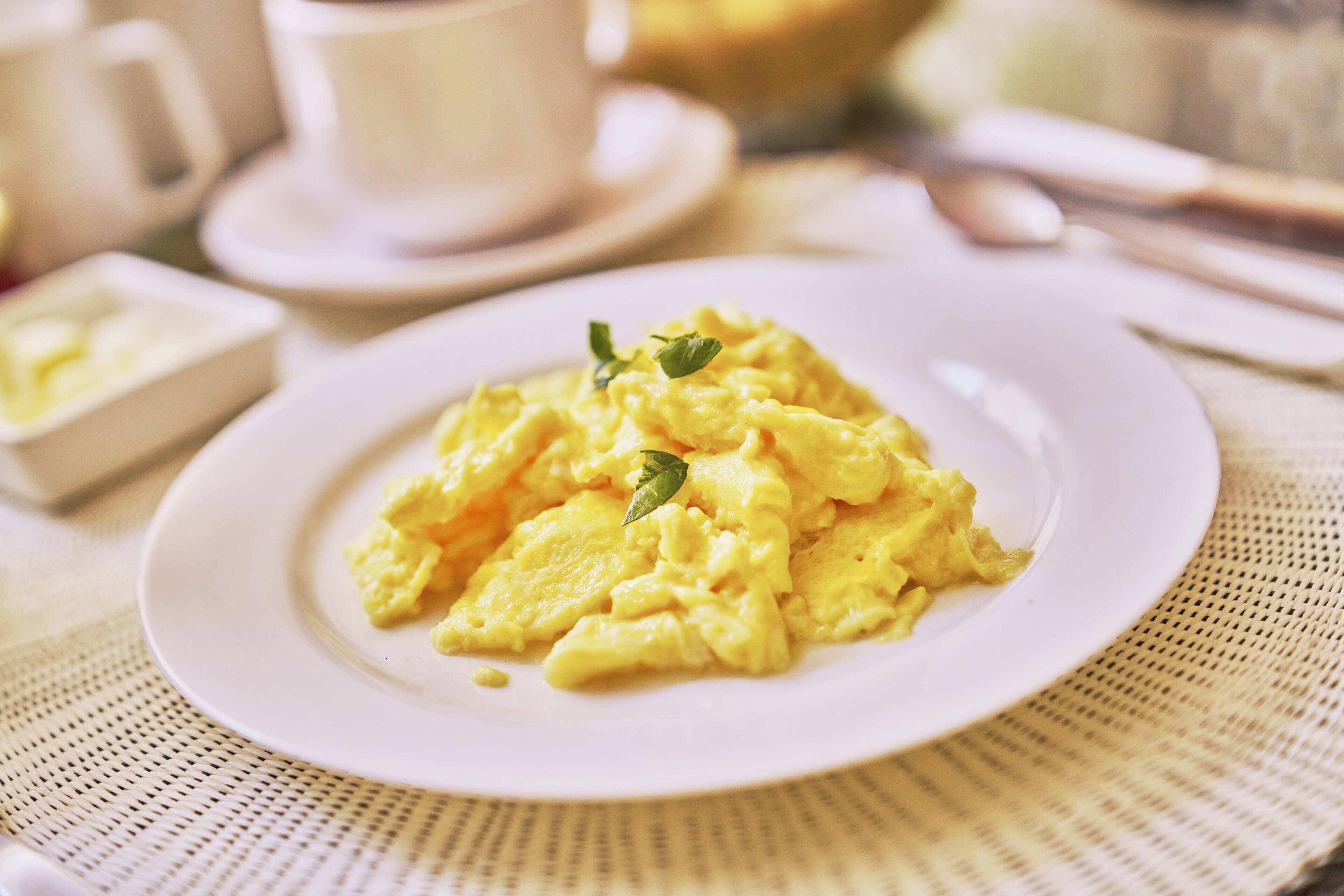 Un plat d'ous barrejats sobre un plat blanc, amb una petita guarnició, damunt d'una taula amb safata.