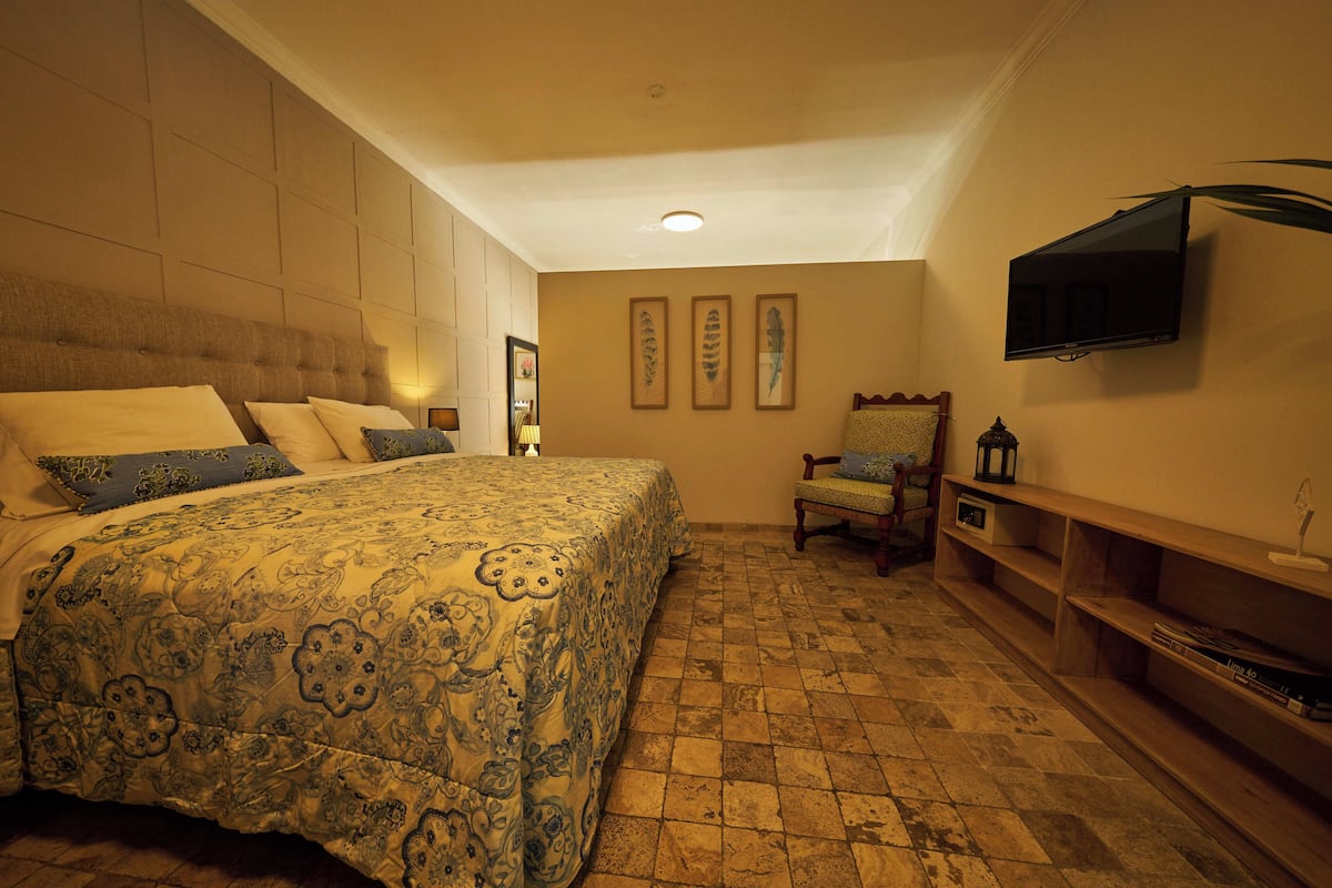 A bedroom with a large bed, a television mounted on the wall, a chair, and a shelf with books.