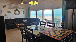 A living room with a sofa, dining table, chairs, and a view of the beach. - Oceanfront 3 bdrm home.  Miramar Escape.  AC, Wi fi, Icemaker.   Beach! (Puerto Penasco)