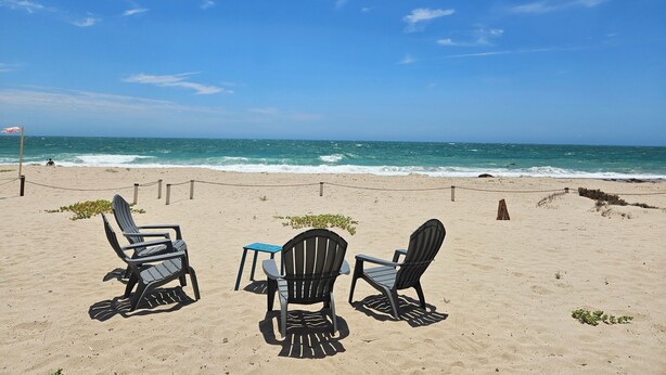 A beach with three Adirondack chairs and a small table under a wooden structure, overlooking the ocean. - Oceanfront 3 bdrm home.  Miramar Escape.  AC, Wi fi, Icemaker.   Beach! (Puerto Penasco)