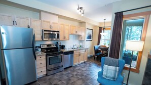 A modern kitchen with stainless steel appliances, wooden cabinets, and a checkered floor. - Relax with a Cozy Private Deck, Warm South Sun and Pool & Hot Tubs. (Canmore)