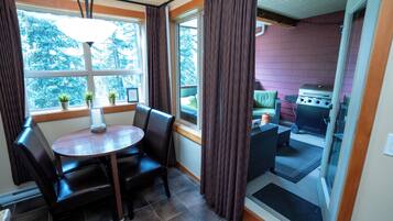 A dining area with a round table and chairs, a window with curtains, and a view of the outdoors.