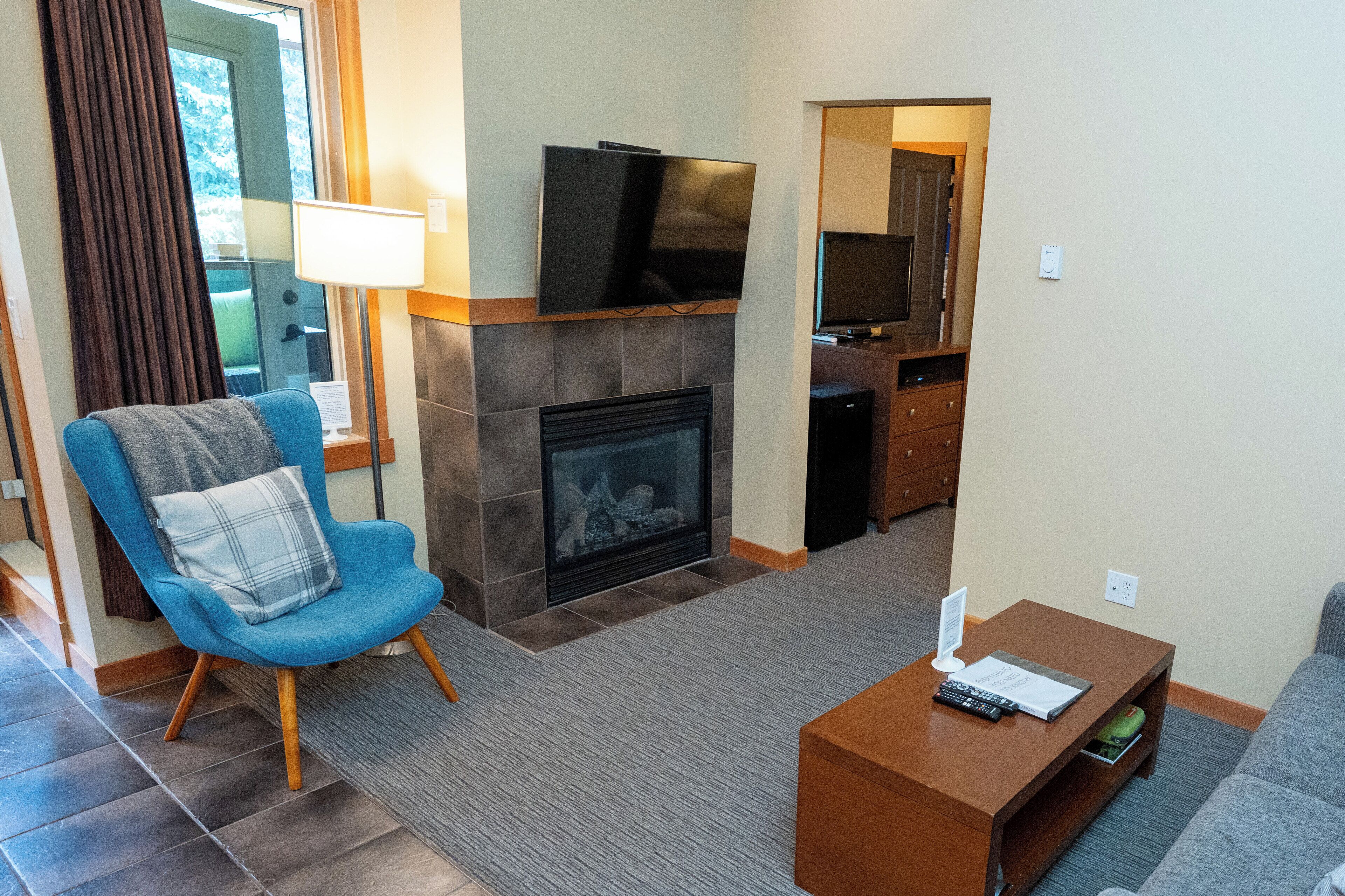 A living room with a blue armchair, a fireplace, a television mounted above it, and a small wooden coffee table.