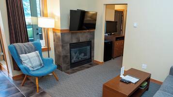 A living room with a blue armchair, a fireplace, a television mounted above it, and a small wooden coffee table.