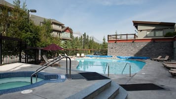 A swimming pool with lounge chairs, a red umbrella, and a stone wall.