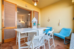 A room with a white table, two white chairs, a blue chair, a white birdhouse, and a wall-mounted heart-shaped decoration.